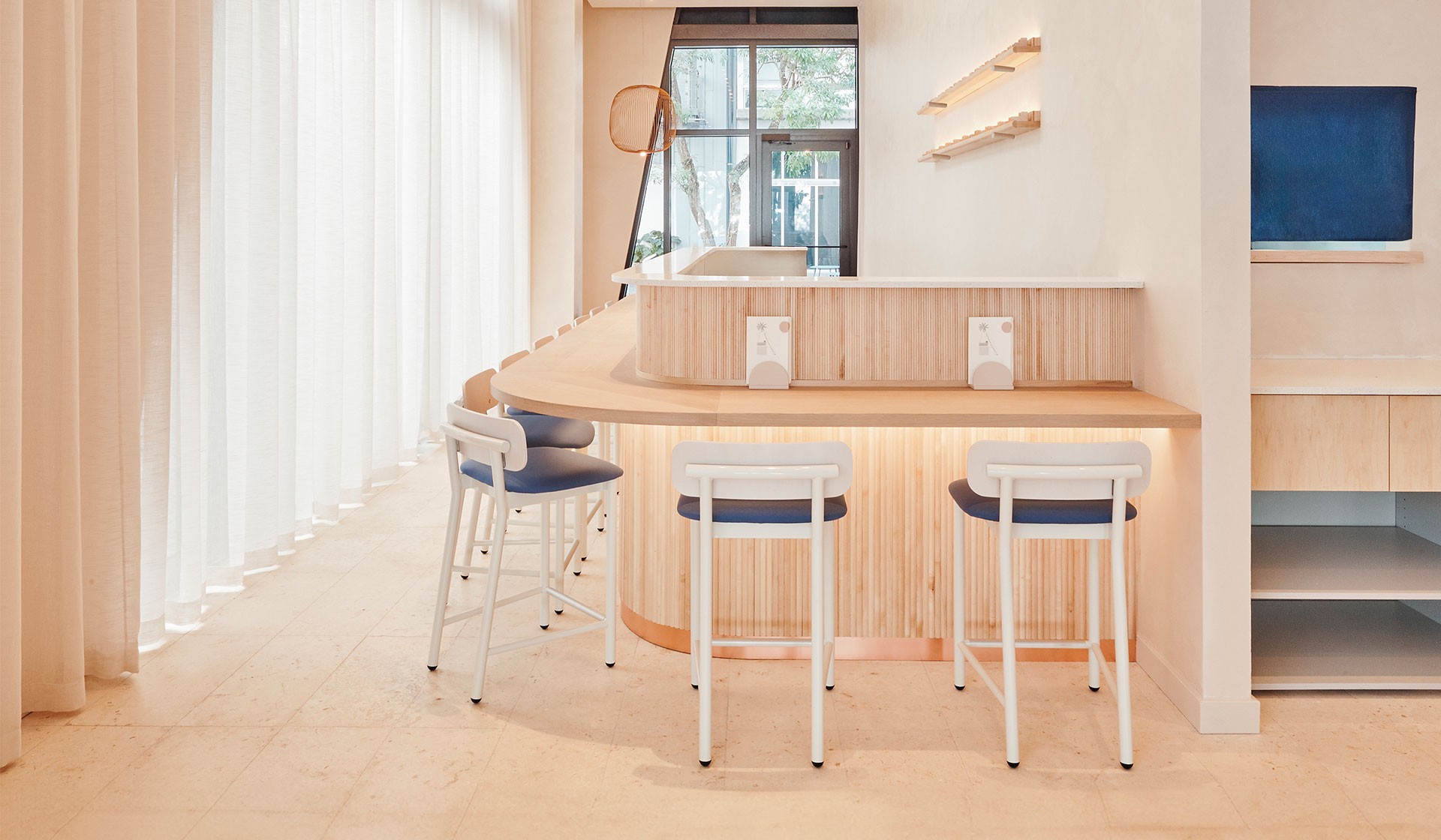 Nami Nori restaurant interior with pale textured walls, a curved timber counter and sheer curtains.